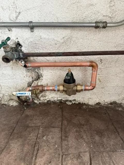Copper piping and valve against a wall, showcasing plumbing system for water supply.