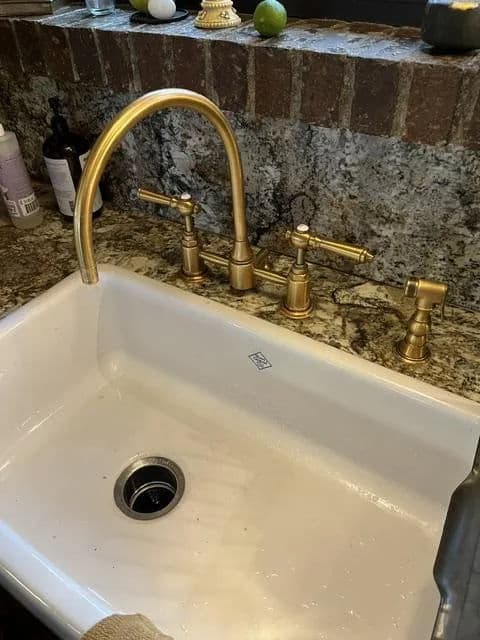 Elegant farmhouse sink with gold faucet and stylish fixtures on a granite countertop.