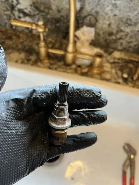 Hand holding a metal plumbing fitting with a threaded end, in a bathroom setting.